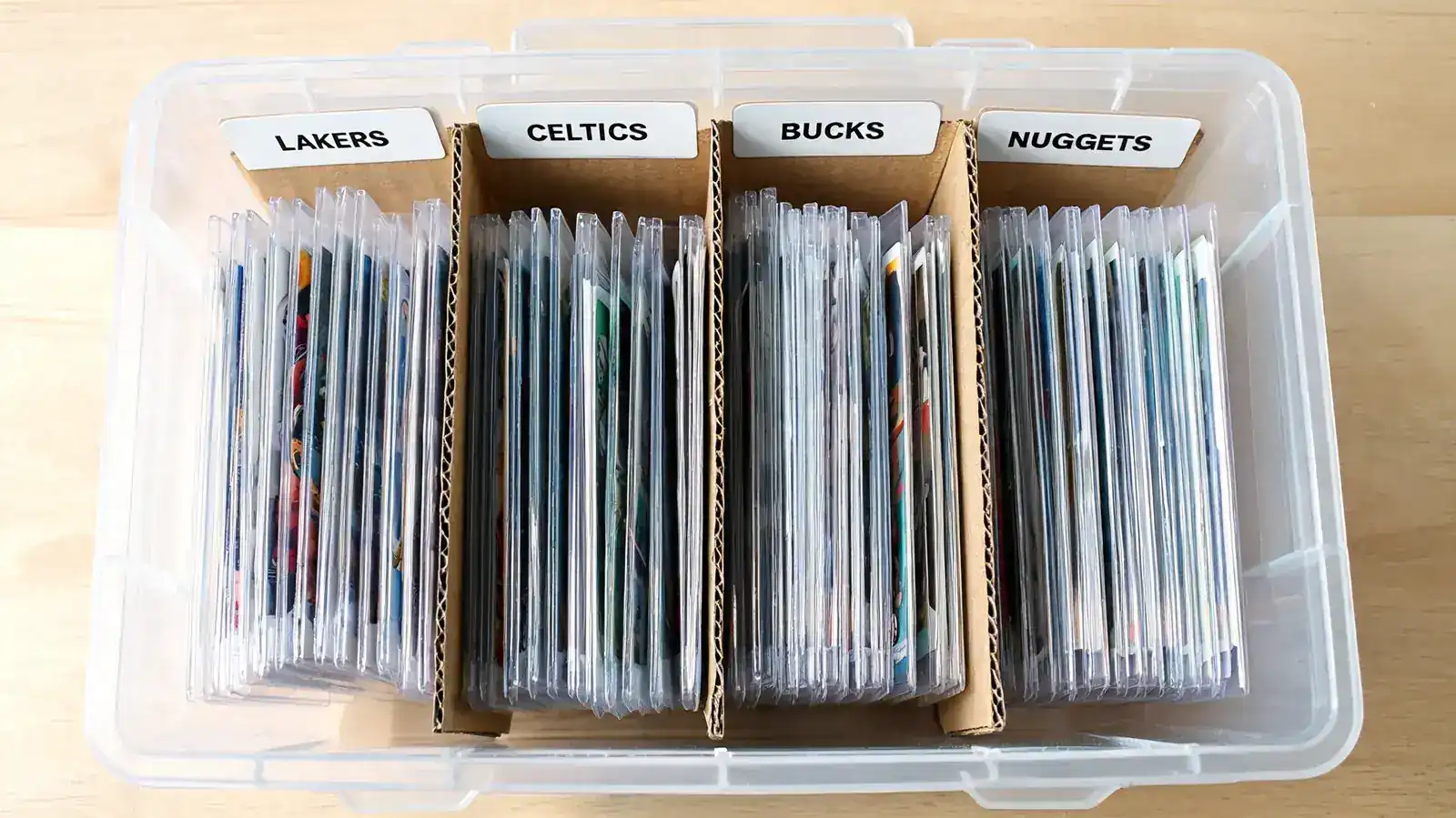 Row of top loaders standing upright inside a BCW storage box divider section, organized by player