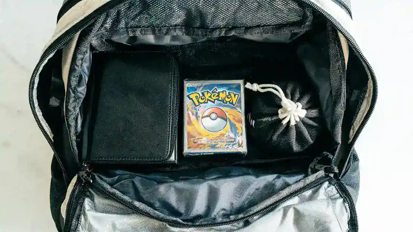 Vault X binder in a backpack alongside a Pokemon tournament kit including dice and a deck box