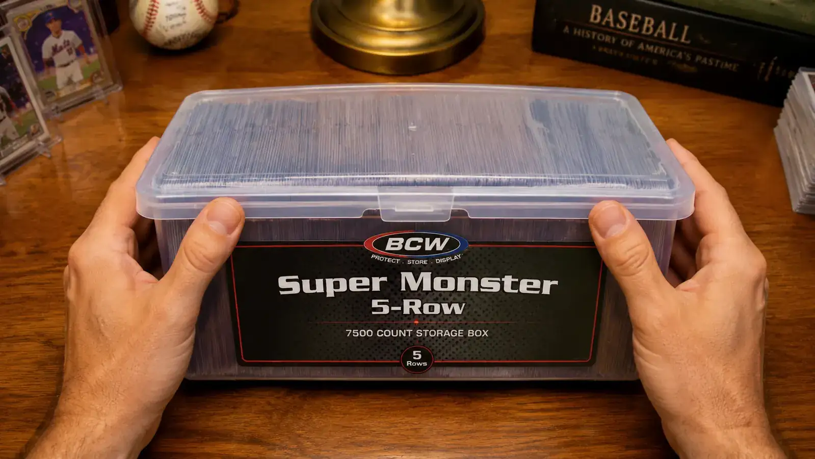 Overhead view of an overstuffed BCW Super Monster box with a visibly bowing lid, cards crammed past the divider line