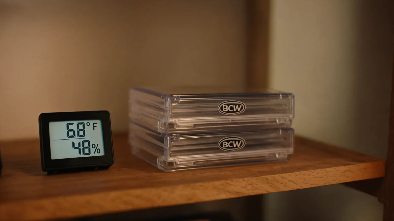 A digital hygrometer on a shelf next to stacked BCW storage boxes showing 48 percent humidity