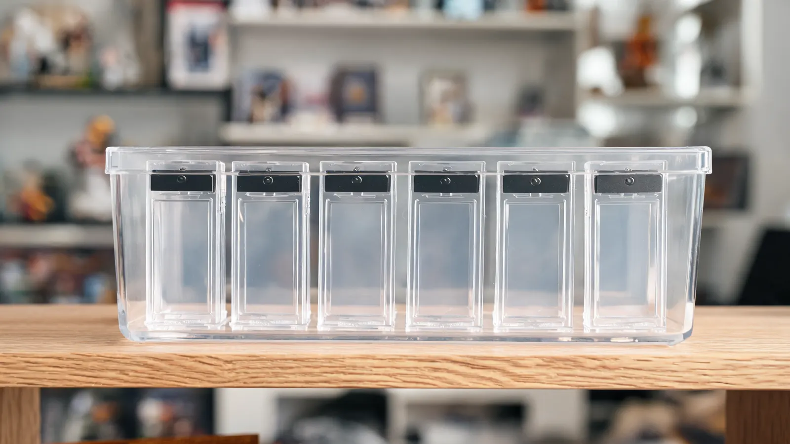 Row of one-touch magnetic holders stored vertically in a clear plastic storage bin on a collector shelf