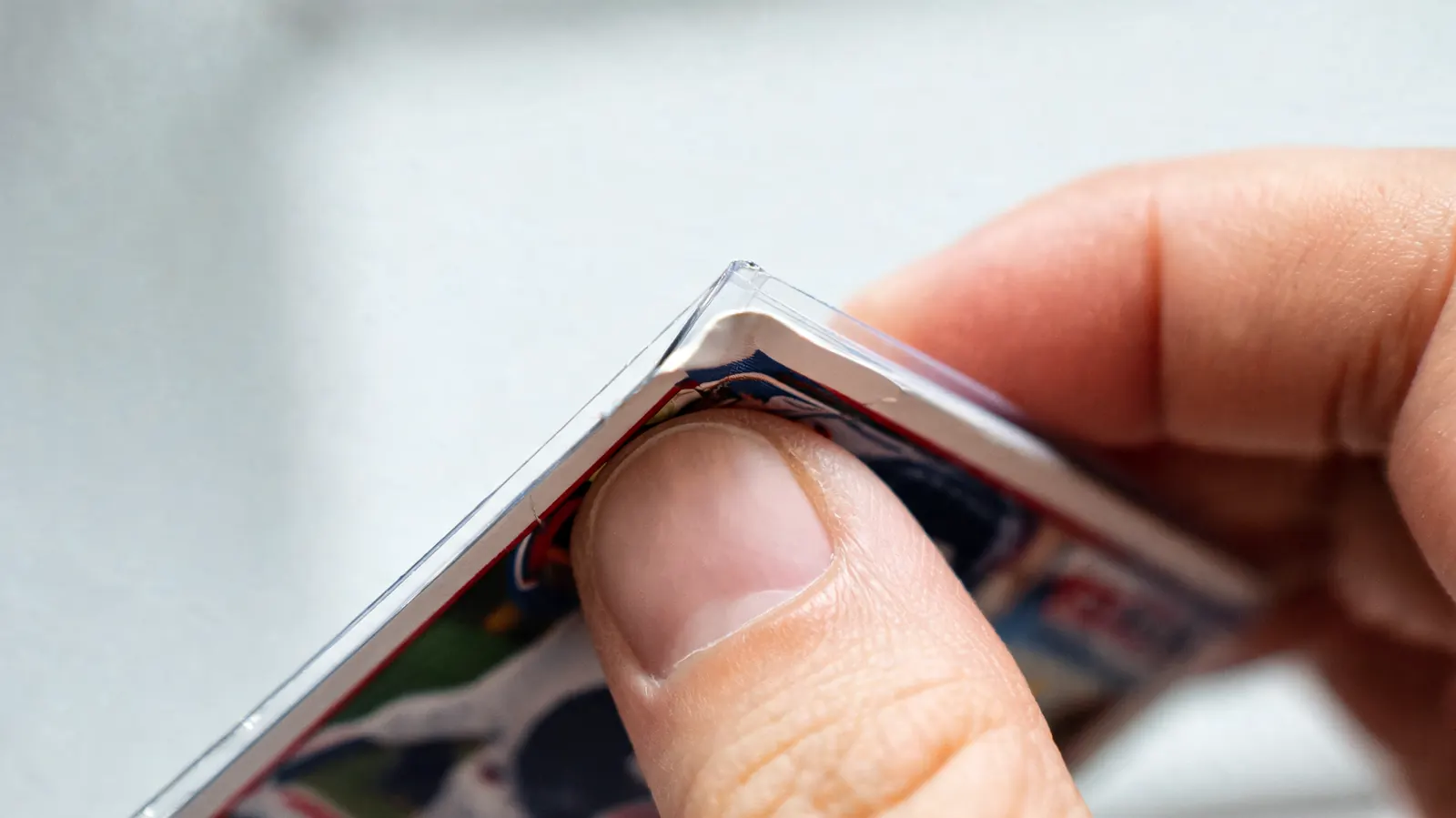 Close-up of a card corner showing a soft bend from being loose in a top loader, held under bright light